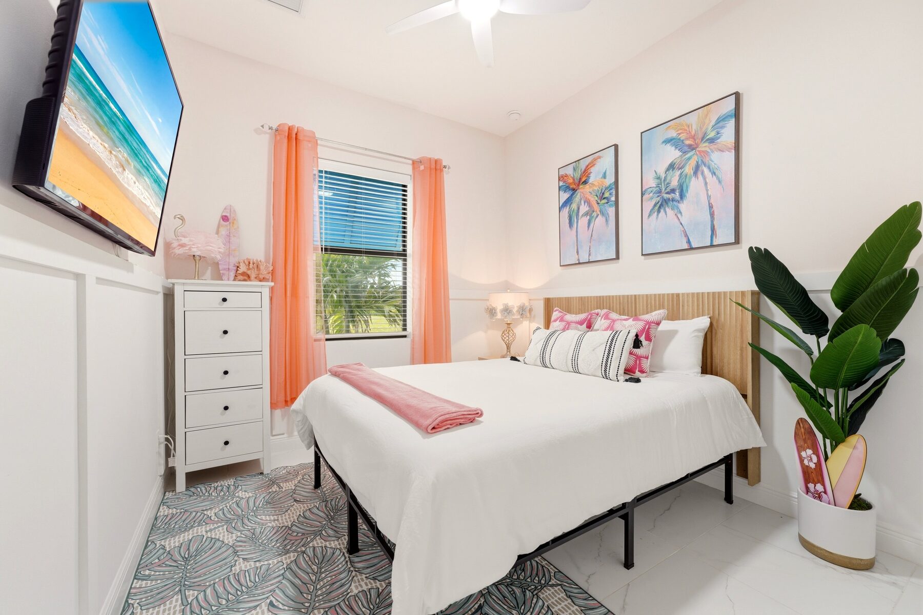 Bright guest bedroom with coral curtains and palm artwork